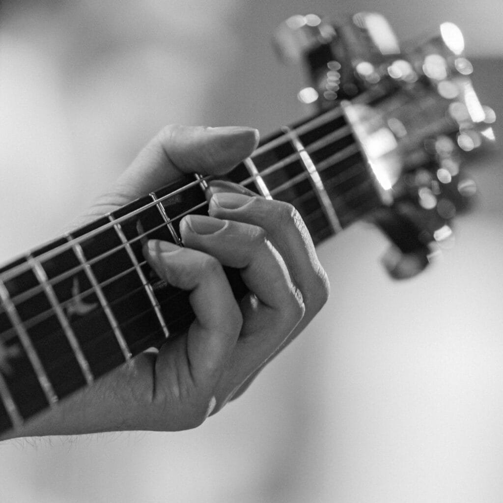 A monochrome close-up of a hand playing a guitar, showcasing musical focus.